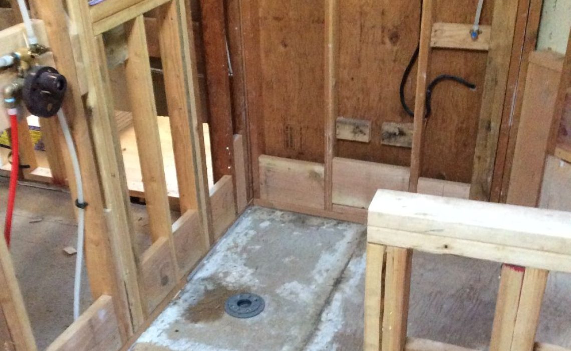 Framed shower area under construction with exposed wooden studs and a concrete shower pan with a central drain