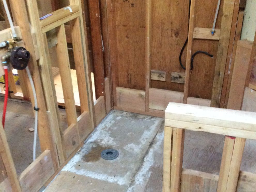 remodeling contractor vs general contractor - Bridgeview Construction Framed shower area under construction with exposed wooden studs and a concrete shower pan with a central drain